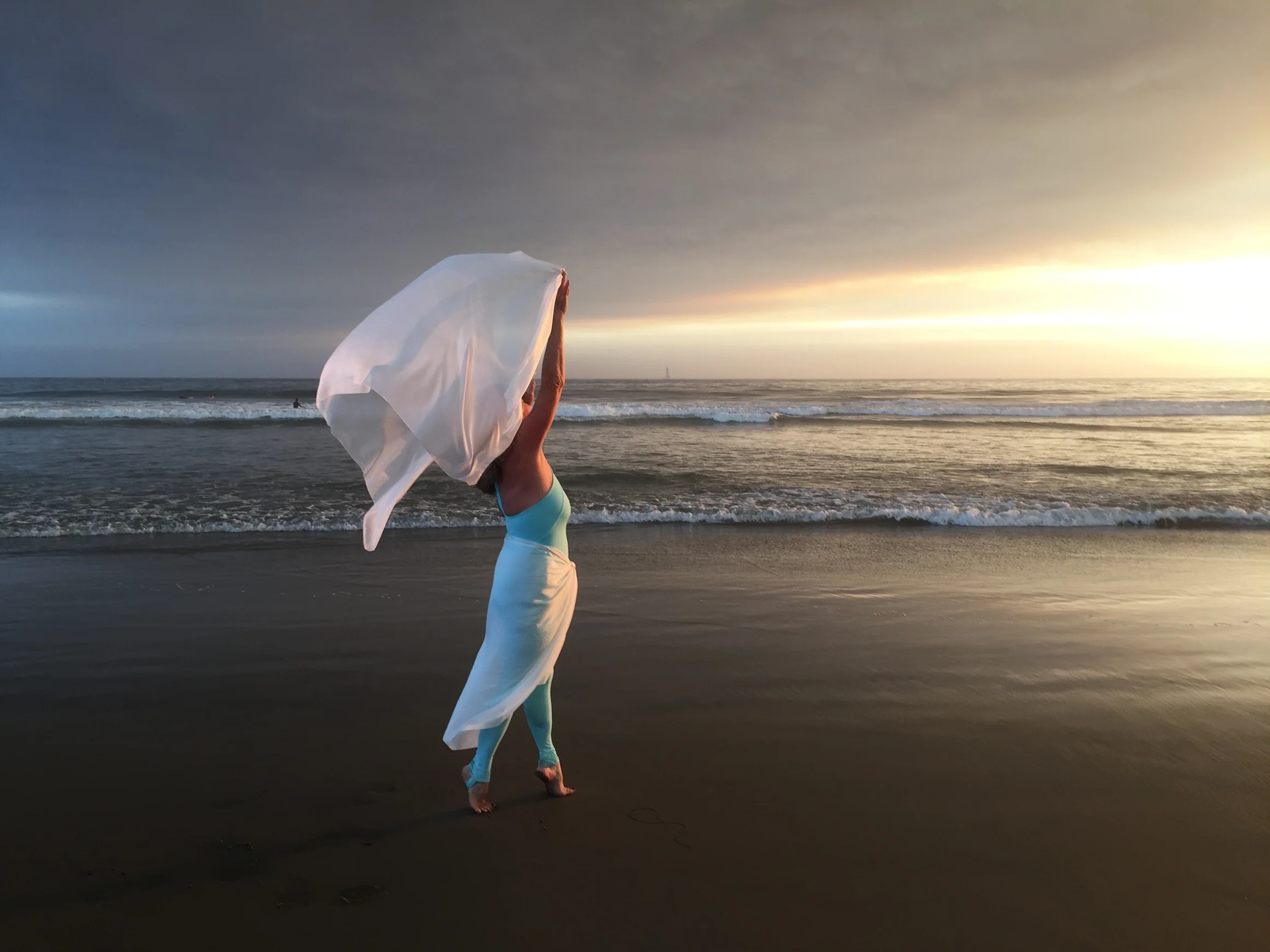 A woman dancing in white fabric at sunset by the ocean